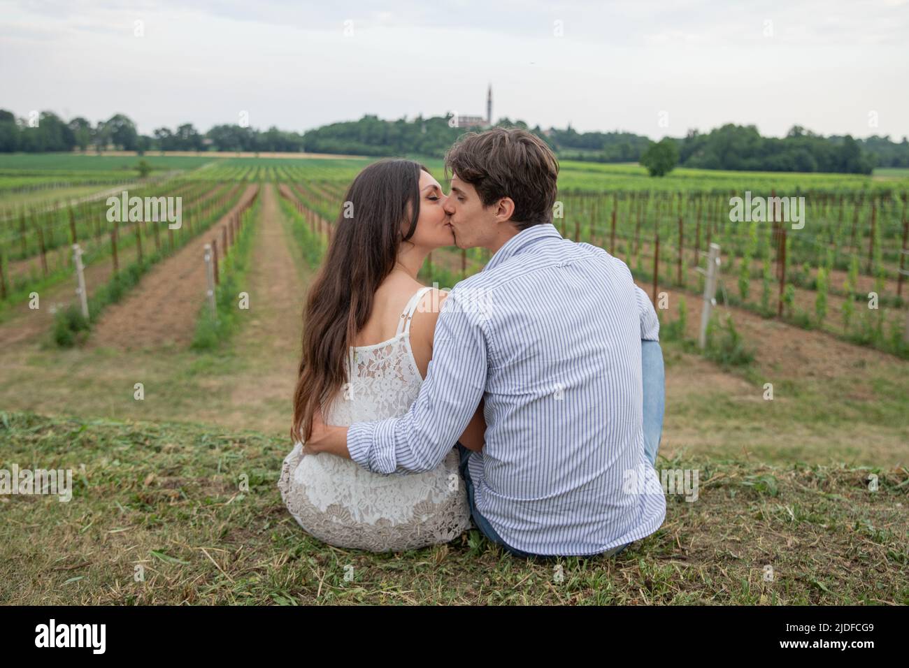 Junges verliebtes Paar sitzt auf dem Gras und küsst sich mitten auf dem Land. Liebeskonzept. Stockfoto