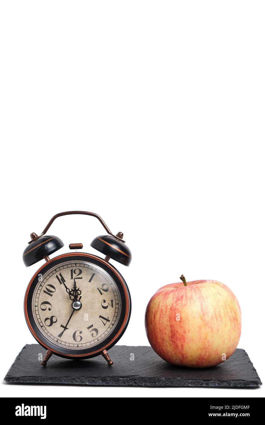 Wecker und Apfel auf Schieferstein auf weißem Hintergrund.Konzept, Zeit haben Snack Stockfoto