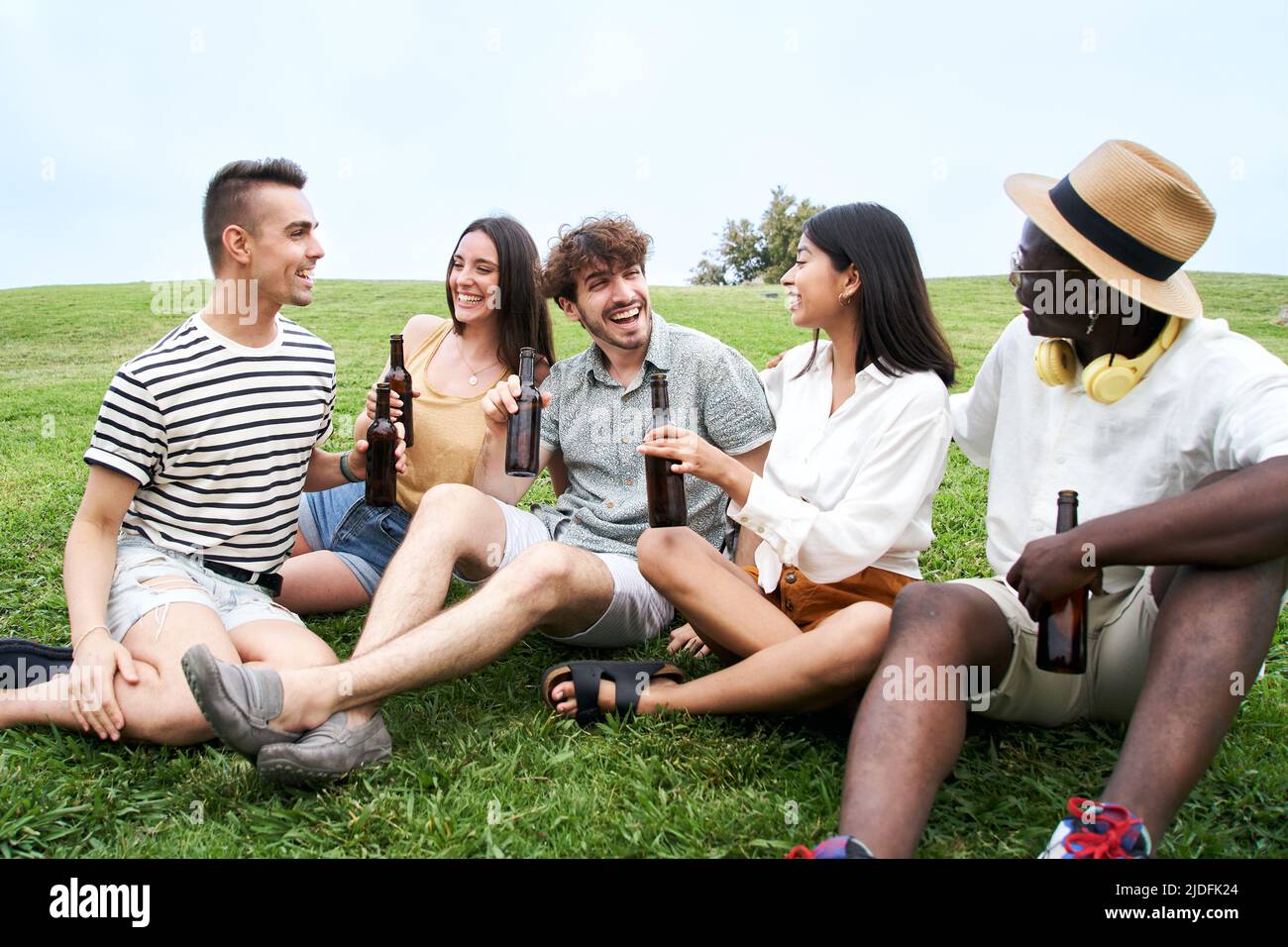 Eine vielfältige Gruppe junger Menschen, die gemeinsam im Freien auf dem Rasen feiern. Freunde, die im Sommer Spaß haben. Stockfoto