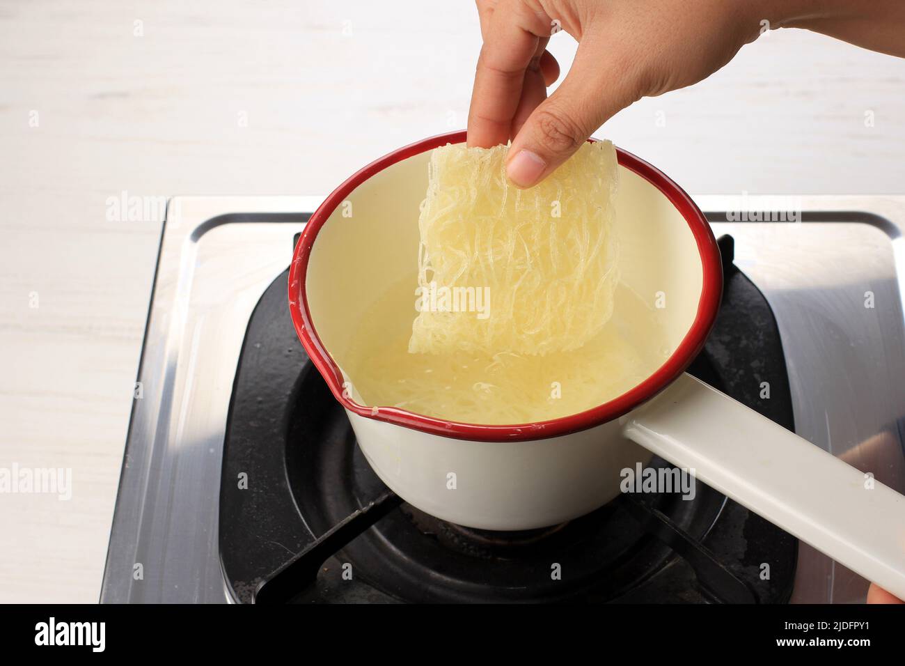 Kochendes Glas oder Reisnudel (Vermicelli) auf einer emaillierten Soße über dem Herd, fügen Sie den Nudel zur Pfanne hinzu, Aktivität zum Kochen nach Hause Stockfoto