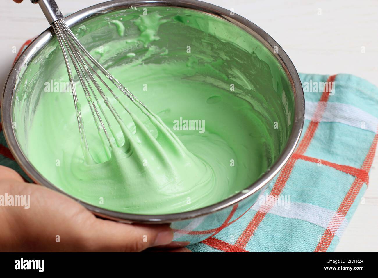 Grünen Teig mit Schneebesen auf der Edelstahlschüssel mischen. Frau hält die Schüssel, den Koch- oder Backvorgang mit der Hand Stockfoto