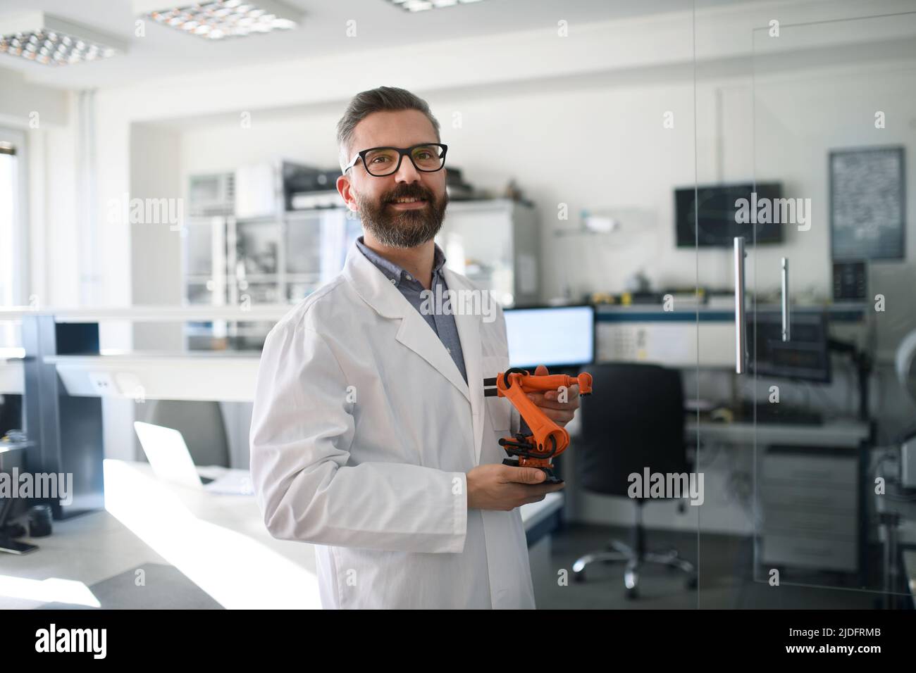 Roboteringenieur hält modernen Roboterarm, steht und blickt in einem Laborbüro auf die Kamera. Stockfoto