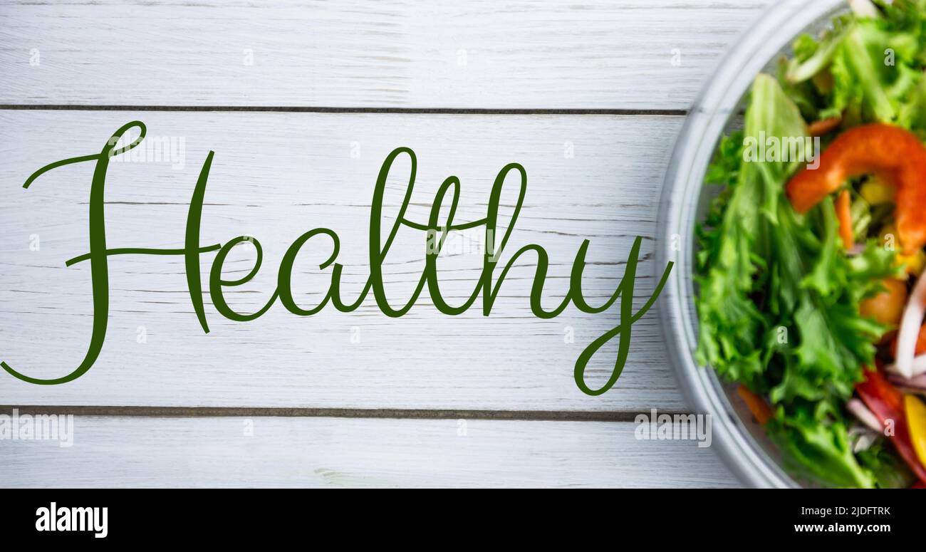 Bild eines gesunden Textes in grün, über frischem Salat in einer Schüssel auf weißen Brettern Stockfoto