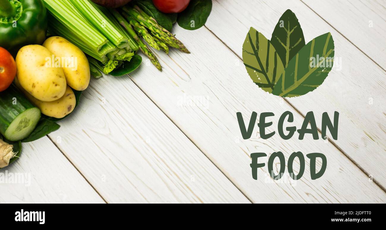 Bild von veganen Lebensmitteln Text in grün, mit Blättern über frischem Gemüse auf weißen Brettern Stockfoto