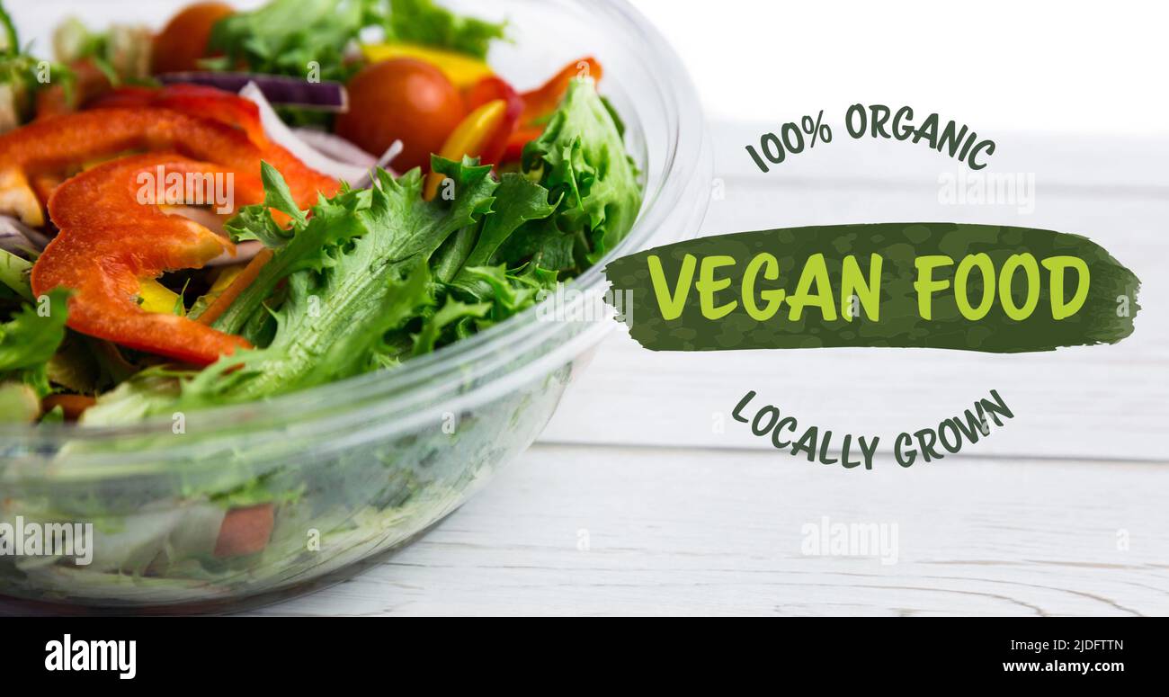 Bild von 100 Prozent Bio-veganen Lebensmitteln Text in grün, über einer Schüssel mit frischem Salat auf weißen Brettern Stockfoto