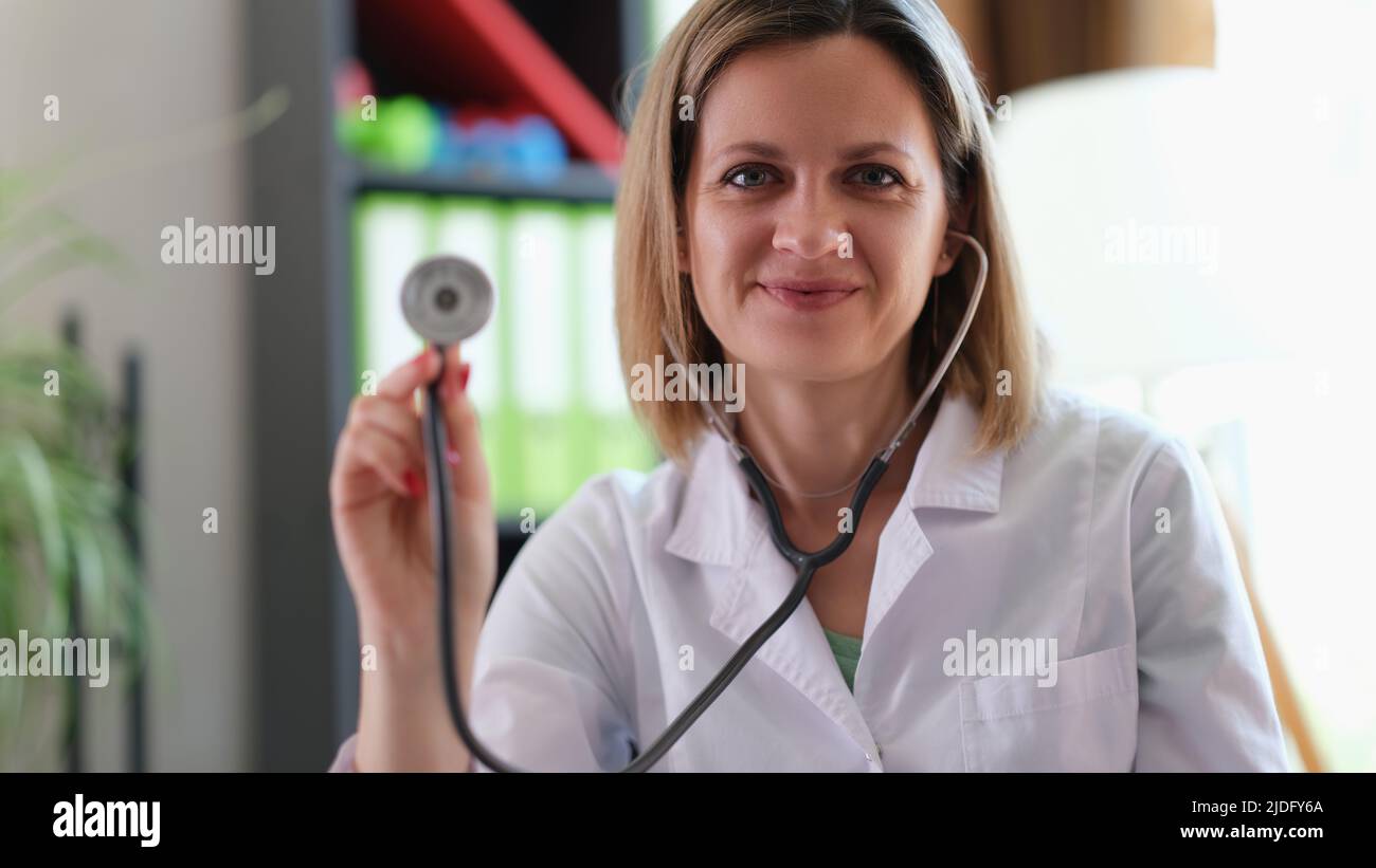 Glücklich lächelnde Praktizierende zeigt medizinisches Stethoskop Stockfoto