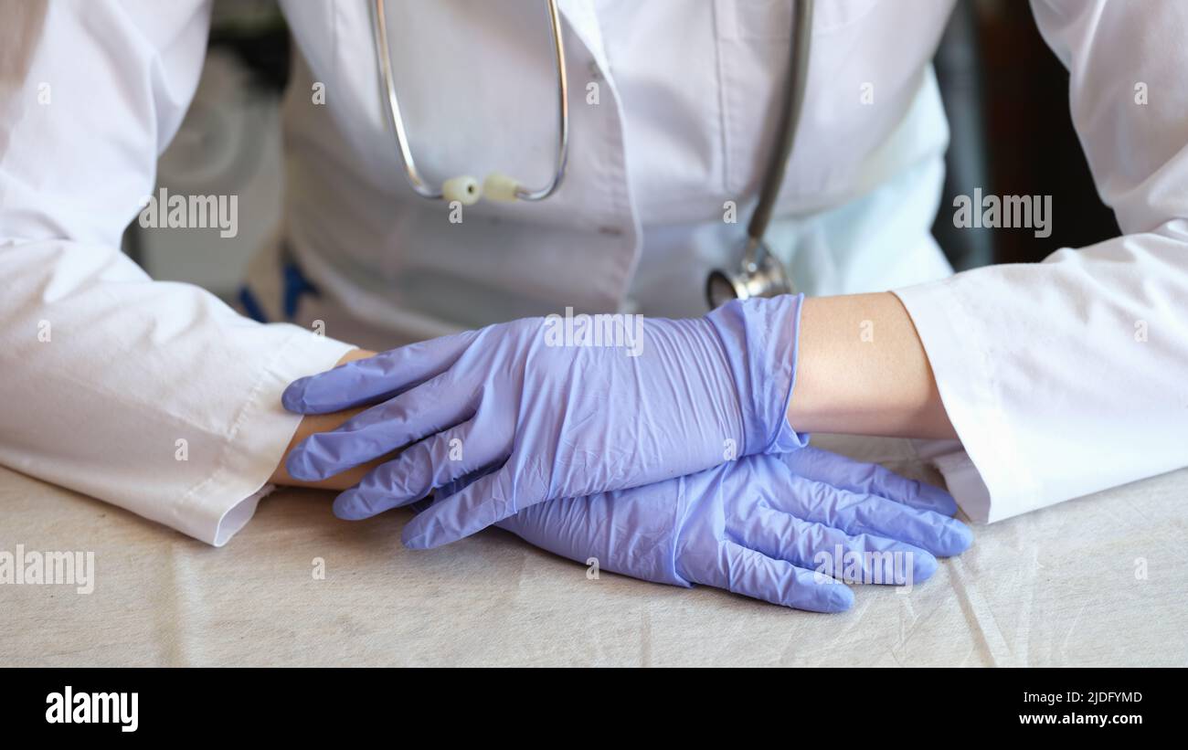 Nahaufnahme einer Ärztin in einem medizinischen Gewand und Handschuhen, die im Klinikbüro posiert. Gesundheits- und Medizinkonzept Stockfoto