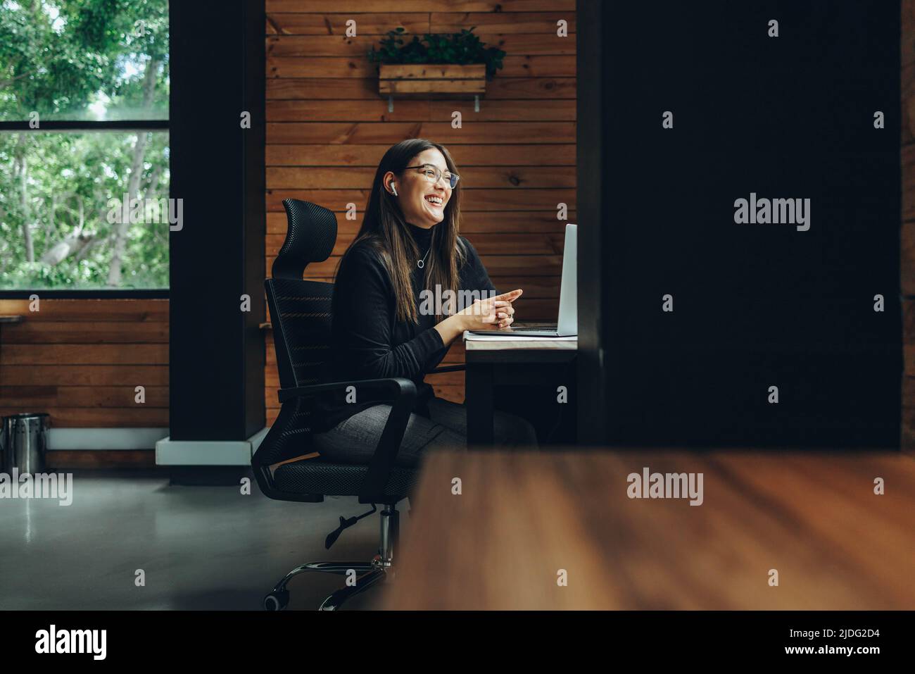Lächelnde Unternehmerin mit einem virtuellen Treffen in einem modernen Co-Working-Raum. Glückliche junge Geschäftsfrau, die mit ihrem Geschäftspartner kommuniziert Stockfoto