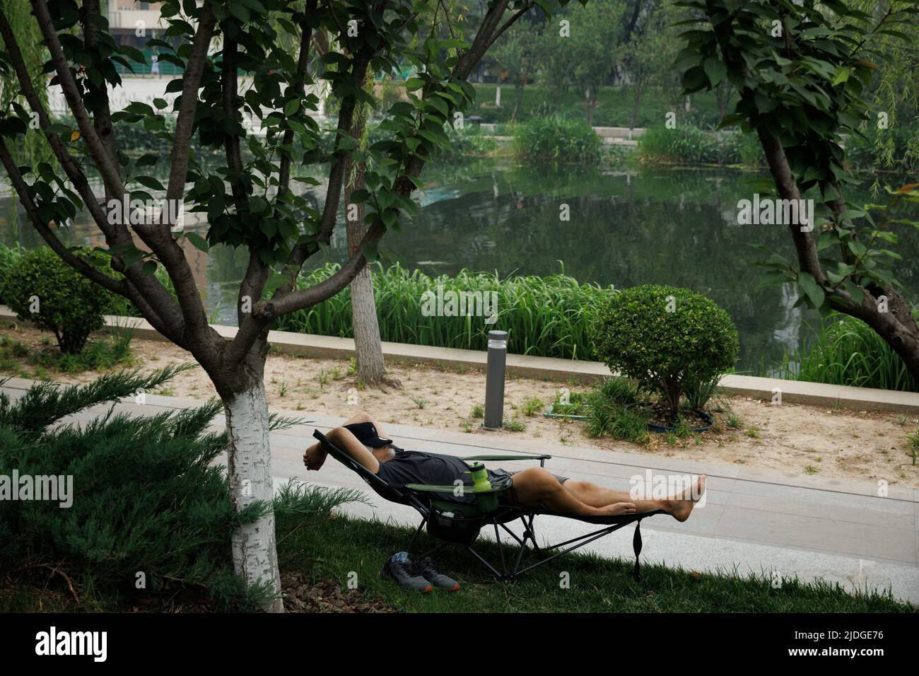 An einem heißen Tag der Sommersonnenwende in Peking, China, am 21. Juni 2022, ruht ein Mann auf einem Campingstuhl an einem Kanal. REUTERS/Thomas Peter Stockfoto