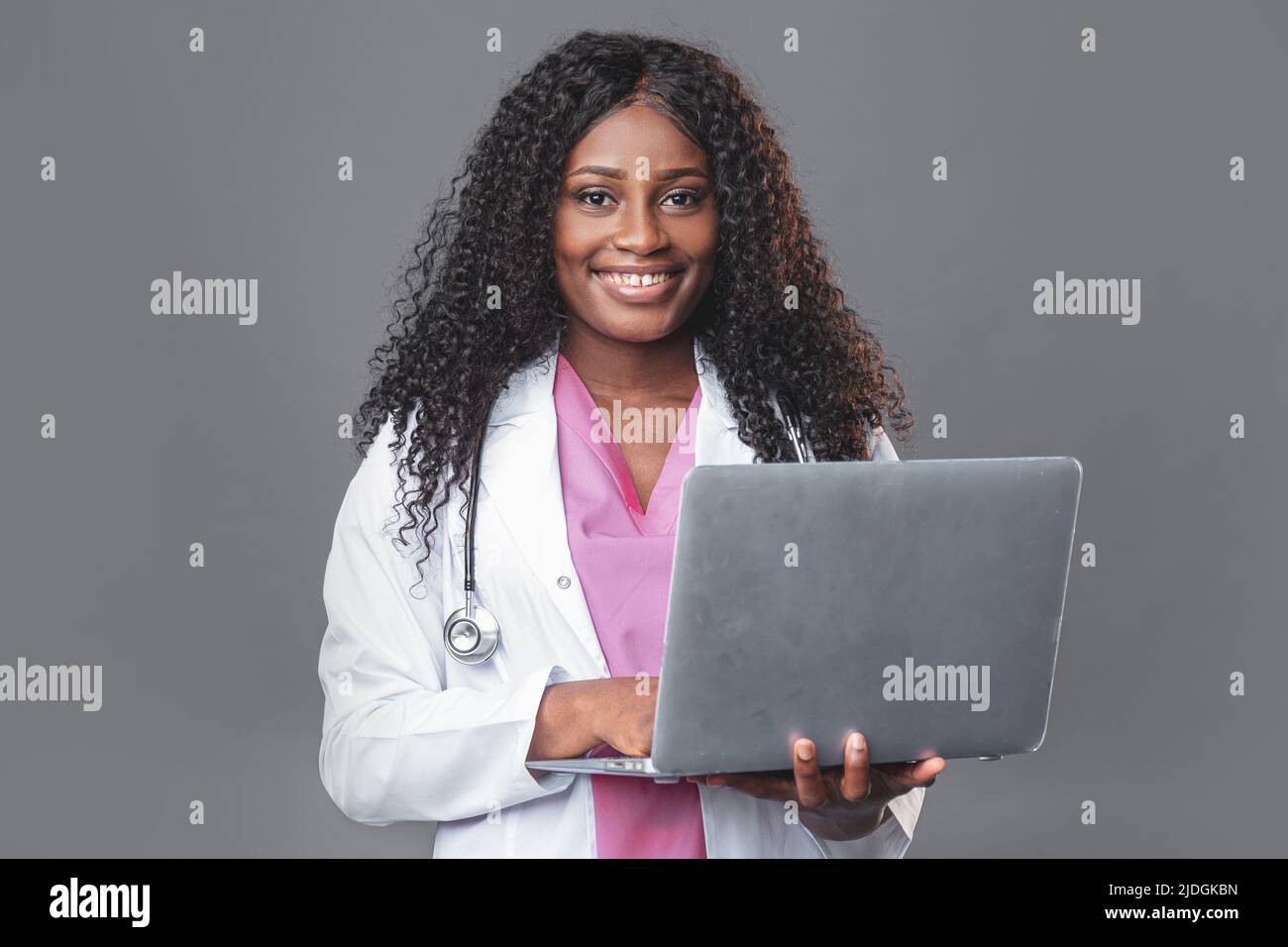 Porträt eines glücklichen professionellen Arztes bei der Arbeit. Eine junge dunkelhäutige Frau in einem weißen Labormantel mit Stethoskop und Laptop steht in einem med Stockfoto