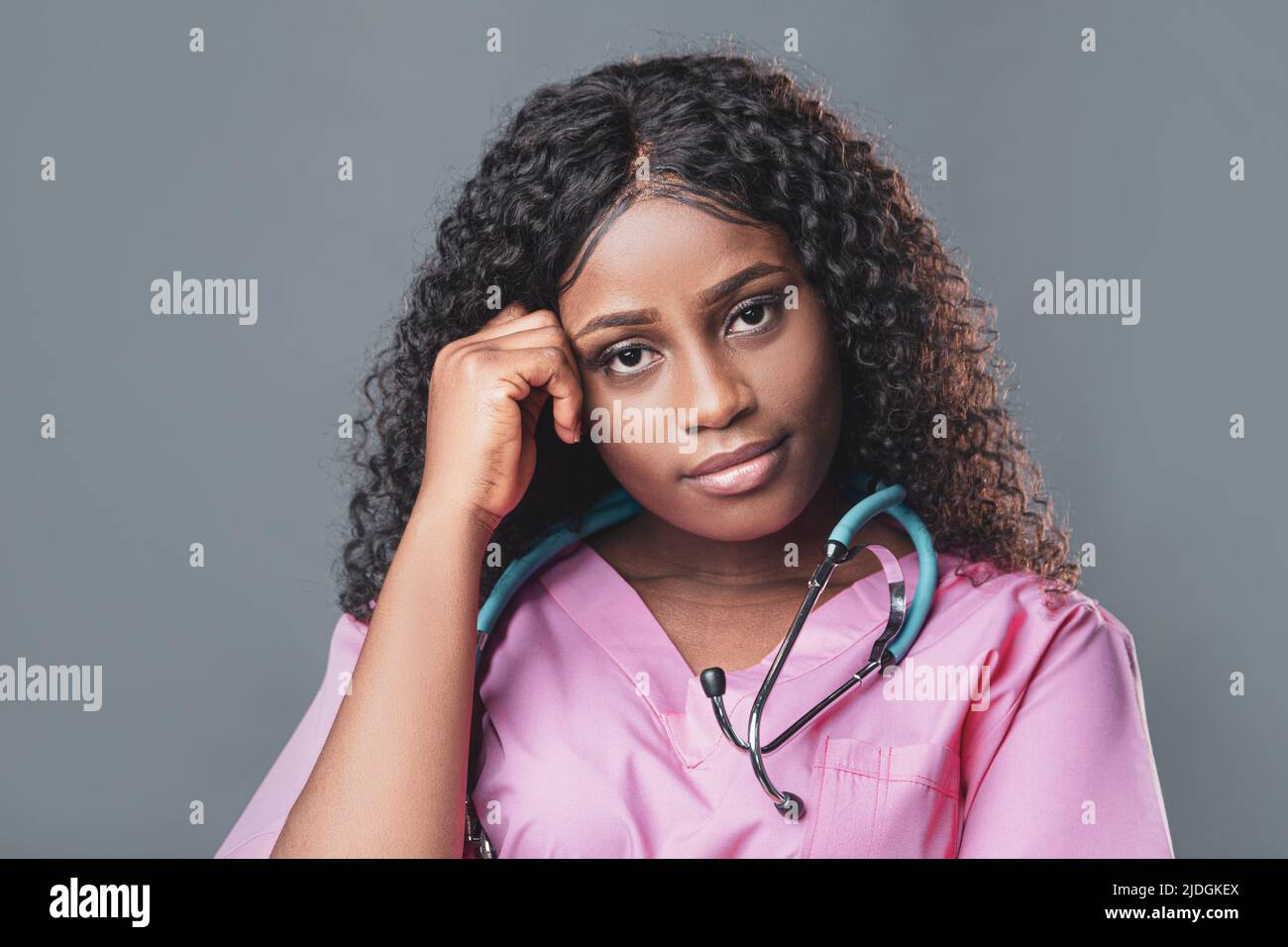 Müde erschöpfte afrikanische Krankenschwester in rosa Uniform auf grauem Hintergrund Stockfoto