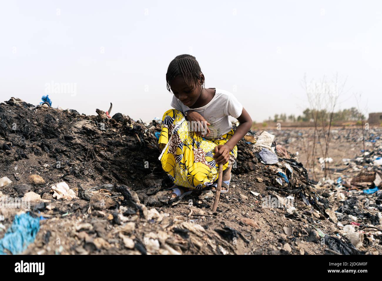 Kleines afrikanisches Mädchen, das auf einem Müllhaufen sitzt und nach recycelbaren Materialien sucht, um ihren bedürftigen Eltern zu helfen Stockfoto