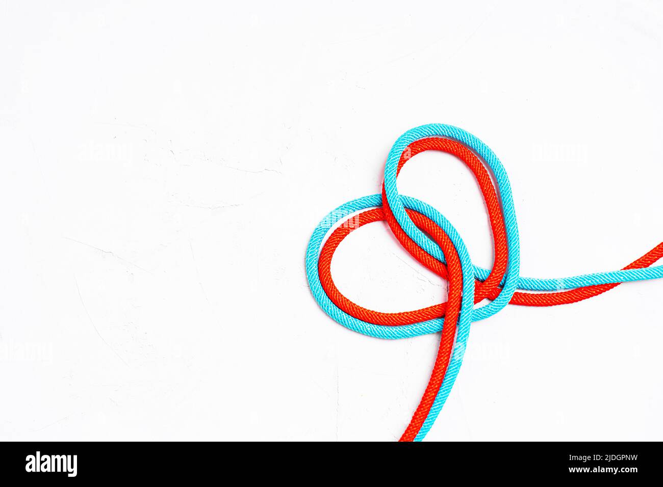 Rote und blaue Schnüre verflochten, um eine Herzform auf grauem Hintergrund zu bilden. Stockfoto
