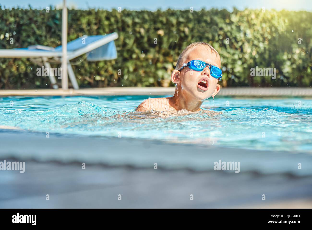 Glücklicher kleiner Junge in der Brille schwimmen in blauem sauberem Wasser Der Außenpool während der Sommerferien im Resort Stockfoto