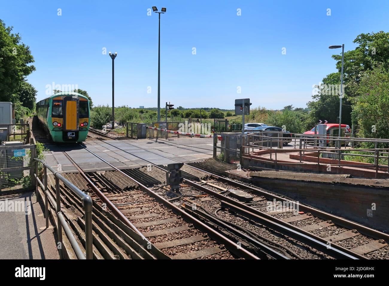 Ford, West Sussex, Großbritannien. Ein Zug des Southern Network überquert den Bahnübergang, während die Autos an der abgesenkten Barriere warten. Stockfoto