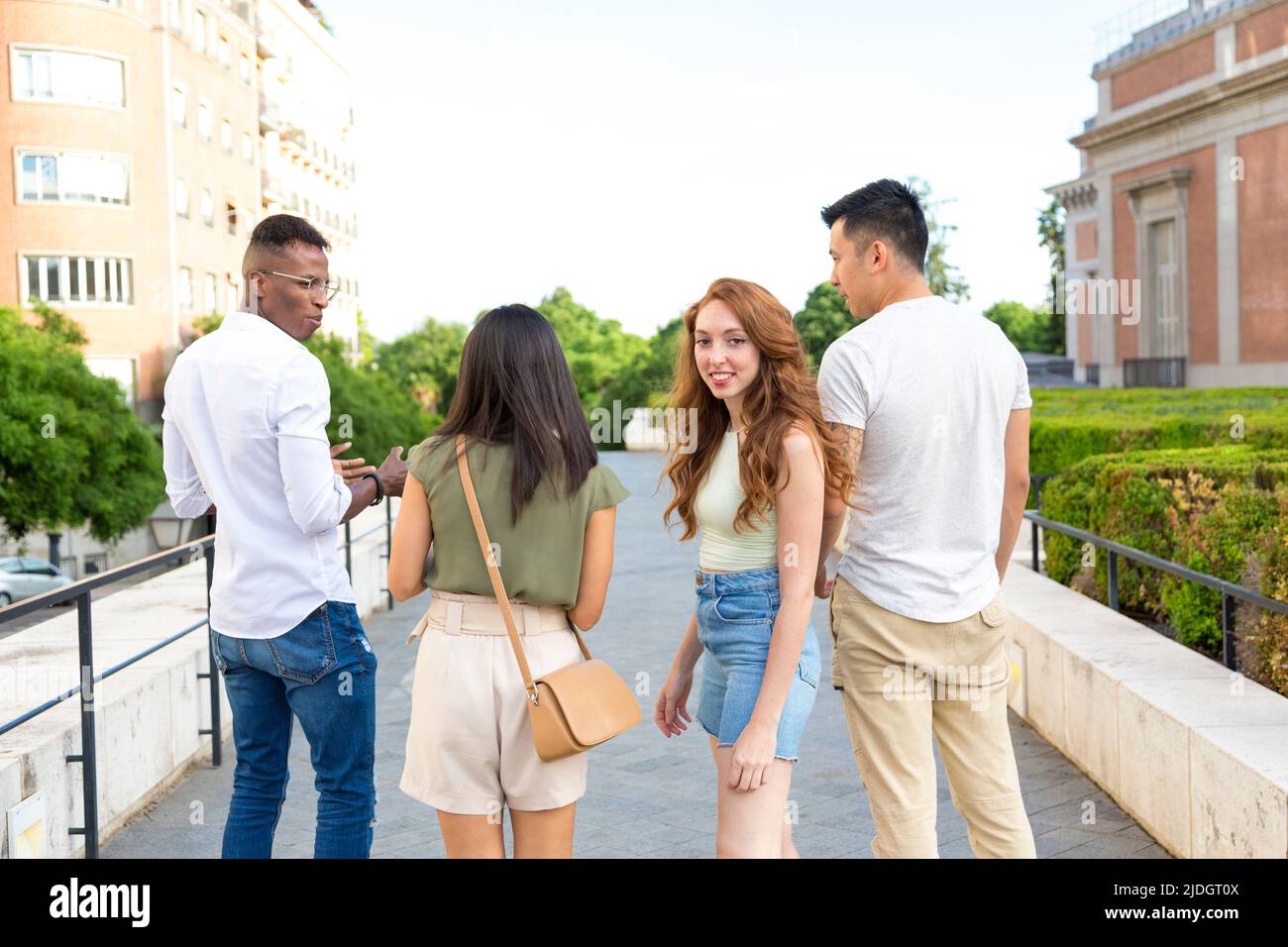 Multiethnische Gruppe von Freunden, die auf der Straße spazieren, während einer von ihnen sich der Kamera zuwendet Stockfoto