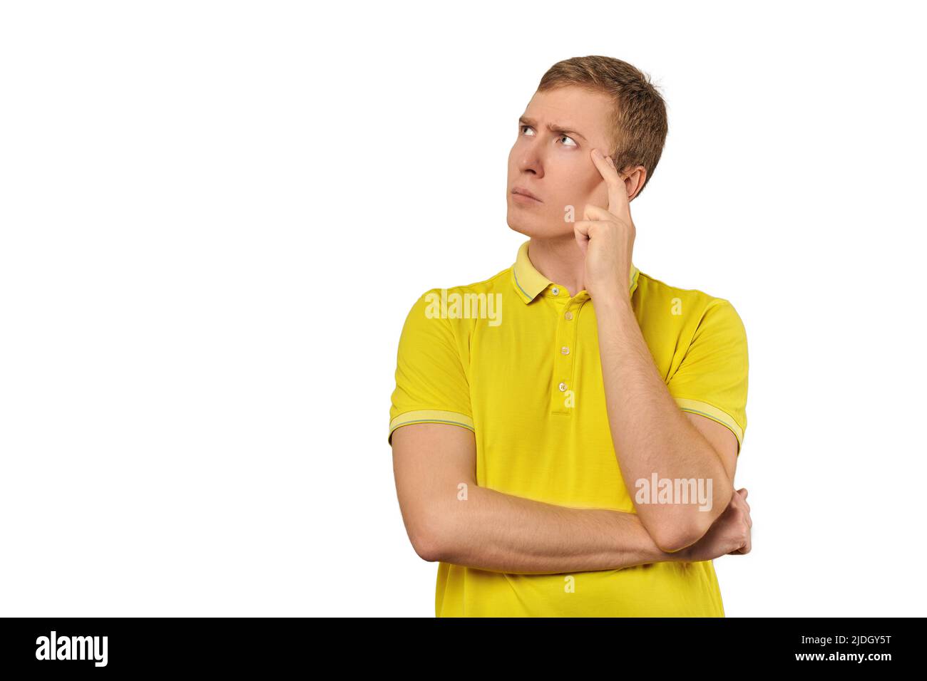 Nachdenklicher Kerl in gelbem T-Shirt, der isoliert auf weißem Hintergrund nach links schaut. Nachdenkender junger Mann, der die Hand an den Kopf legt und darauf schaut Stockfoto