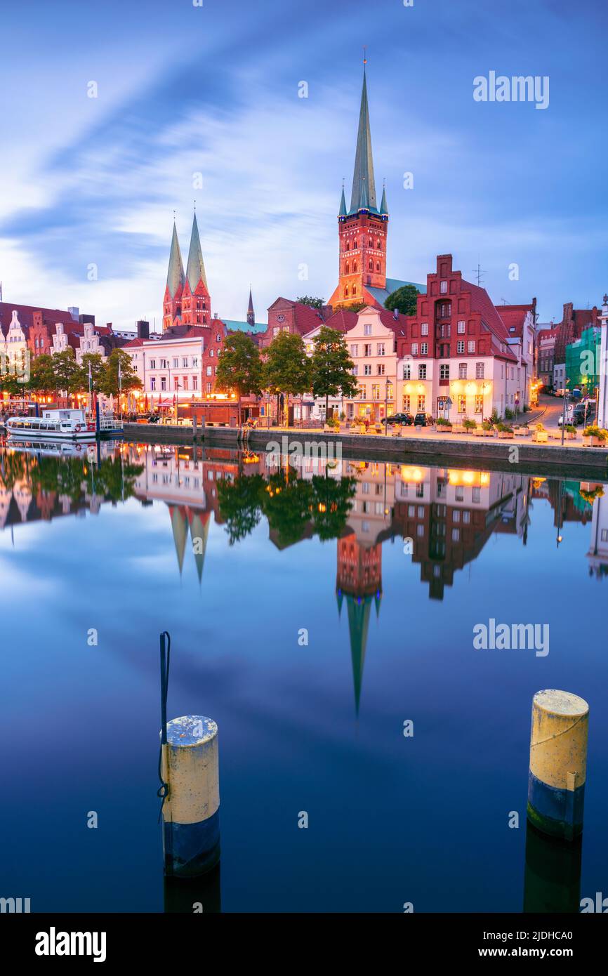 Lübeck, Deutschland. Stadtbild des Lubecker Flussufers mit Spiegelung der Stadt im Trave bei Sonnenuntergang. Stockfoto