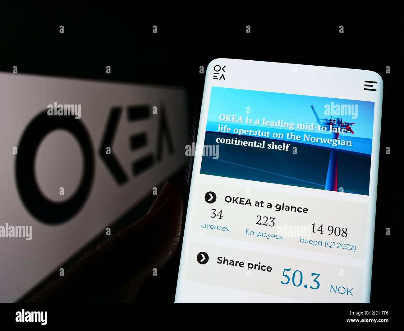 Person, die Mobiltelefon mit der Website des norwegischen Ölunternehmens OKEA ASA auf dem Bildschirm vor dem Unternehmenslogo hält. Konzentrieren Sie sich auf die Mitte des Telefondisplays. Stockfoto