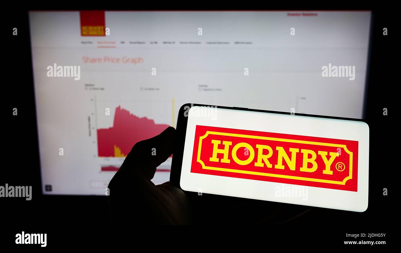 Person, die ein Mobiltelefon mit dem Logo der britischen Modelleisenbahngesellschaft Hornby plc auf dem Bildschirm vor der Unternehmenswebseite hält. Konzentrieren Sie sich auf die Telefonanzeige. Stockfoto