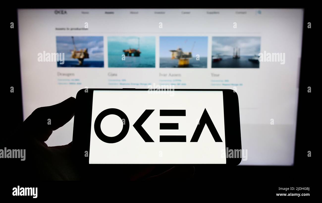 Person, die ein Mobiltelefon mit dem Logo des norwegischen Ölunternehmens OKEA ASA auf dem Bildschirm vor der Unternehmenswebseite hält. Konzentrieren Sie sich auf die Telefonanzeige. Stockfoto