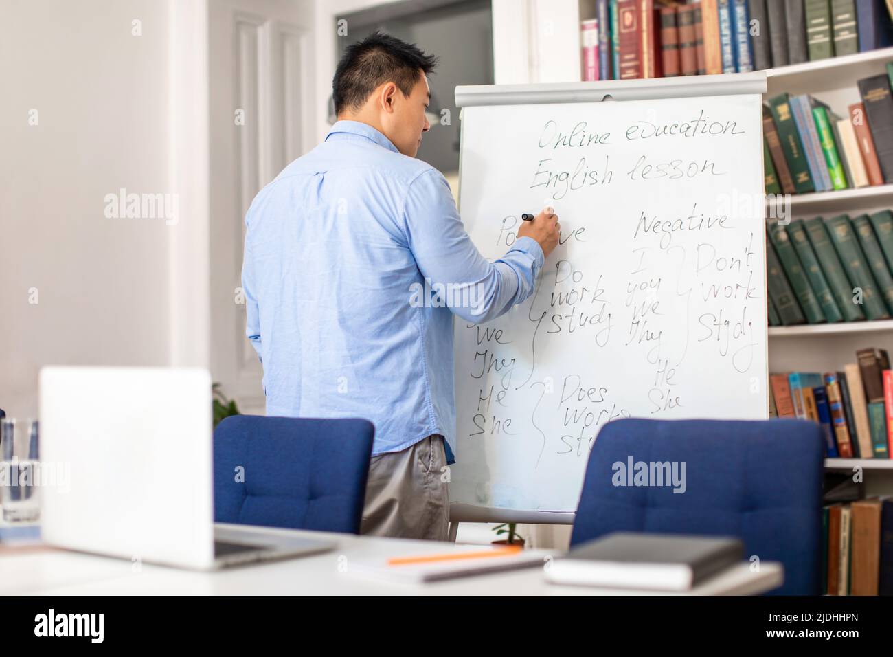 Asian Teacher Man Writing On Whiteboard In Classroom, Back View Stockfoto