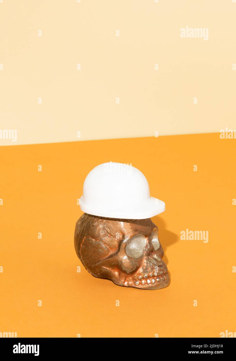 Totenkopf mit weißem Schutzhelm auf orangefarbenem Hintergrund. Schutzzubehör für Bauarbeiter. Halloween oder Santa Muerte Konzept mit Kopie-SPAC Stockfoto