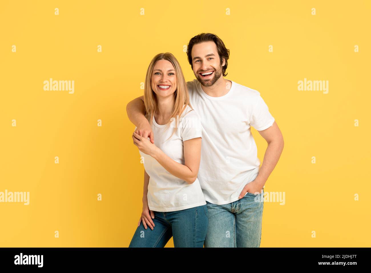 Fröhlicher, froher, tausendjähriger kaukasischer Mann umarmte die blonde Dame in weißen T-Shirts und schaute auf die Kamera Stockfoto