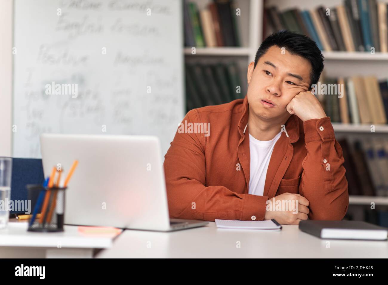 Unglücklicher Asiatischer Lehrer, Der Am Arbeitsplatz Sitzt Und Im Klassenzimmer Probleme Hat Stockfoto