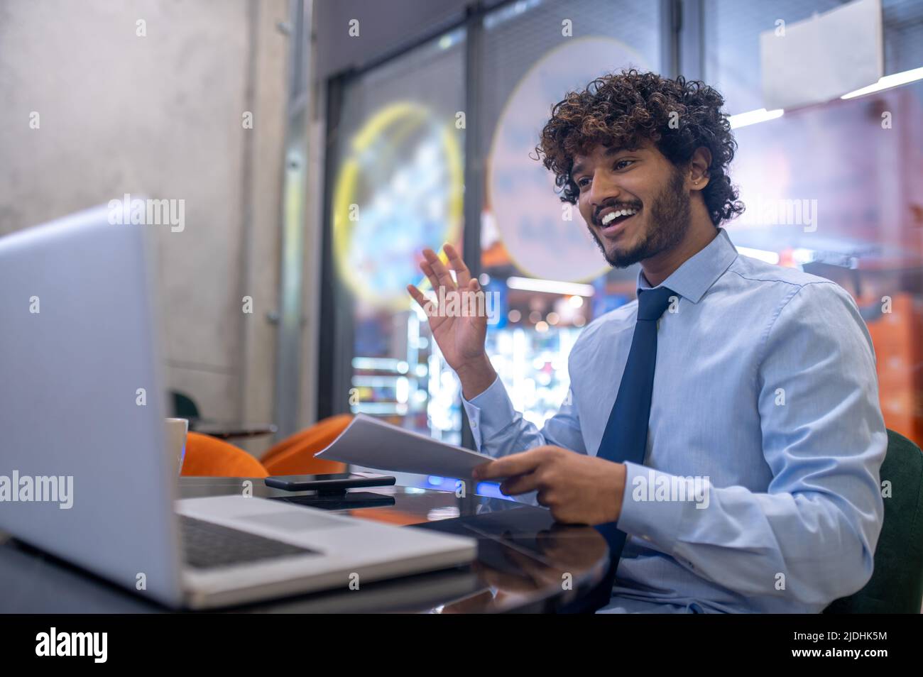 Der Mann stikuliert zur Begrüßung und schaut auf den Laptop, der im Büro sitzt Stockfoto
