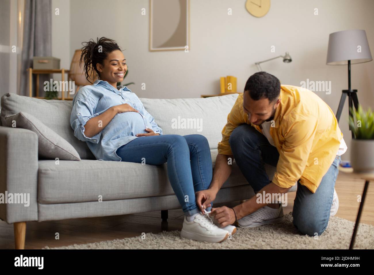 Liebevoller Afroamerikanischer Ehemann Hilft Schwangeren Frau Schnürschuhe Im Innen Stockfoto