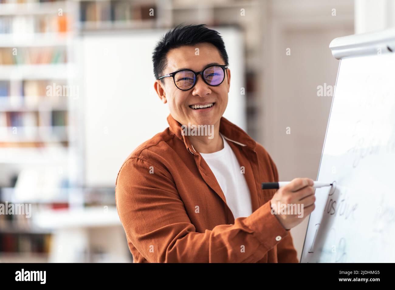 Positive Asiatische Lehrer Mann Lächelnd Schreiben Auf Whiteboard Im Klassenzimmer Stockfoto