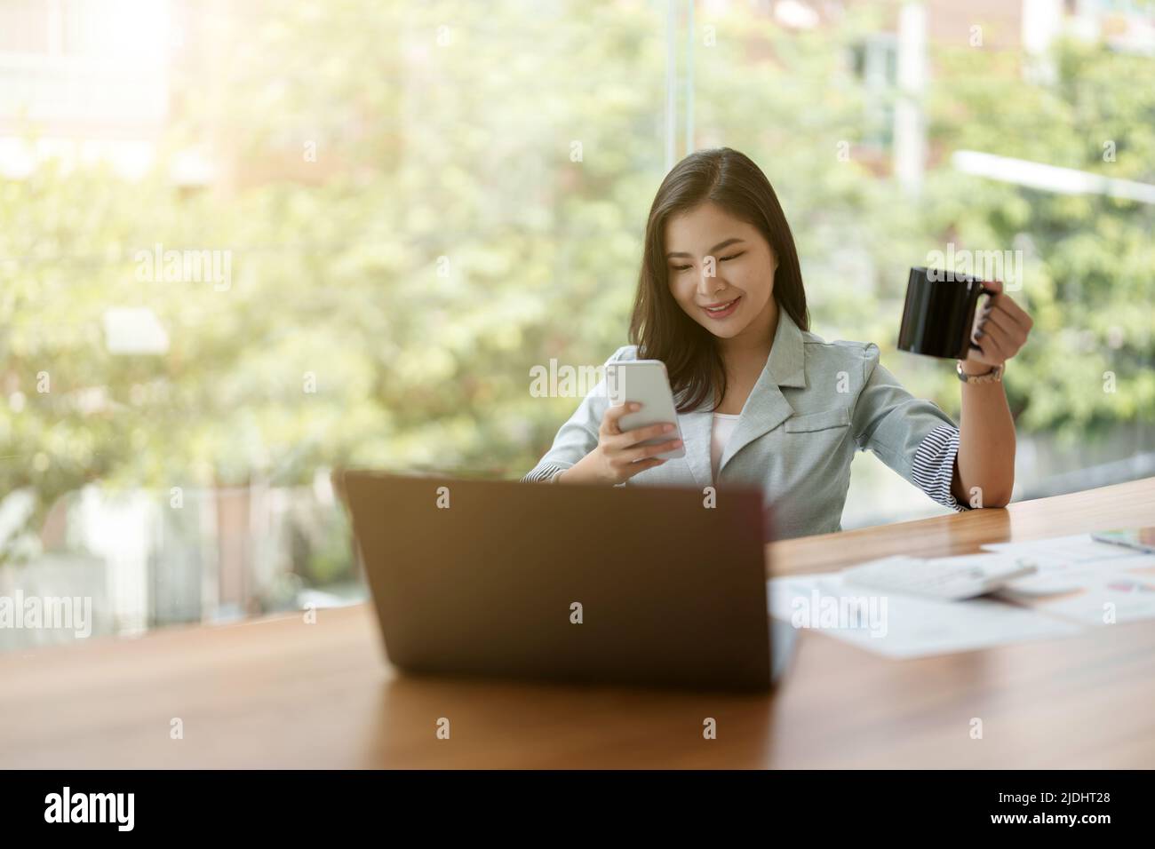 Schöne junge asiatische Geschäftsfrau mit Telefon während der Arbeit mit Rechner und finanzielle Papiere im Büro Stockfoto