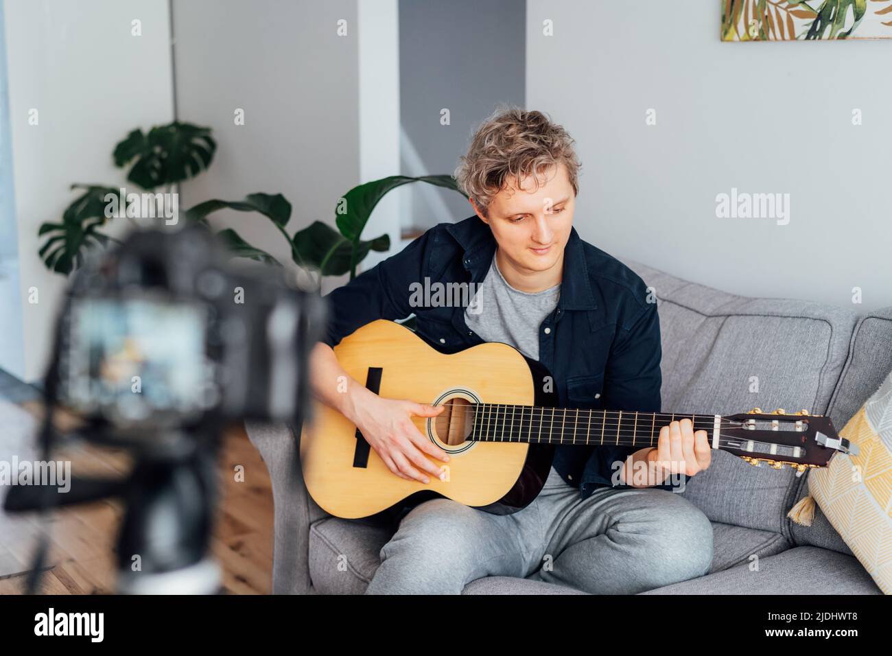 Junger Mann spielt akustische Gitarre und zeichnet Musikvideos für seine sozialen Netzwerke auf. Amatuer Musiker schaffen Inhalte zu Hause mit moderner Kamera. Musicia Stockfoto