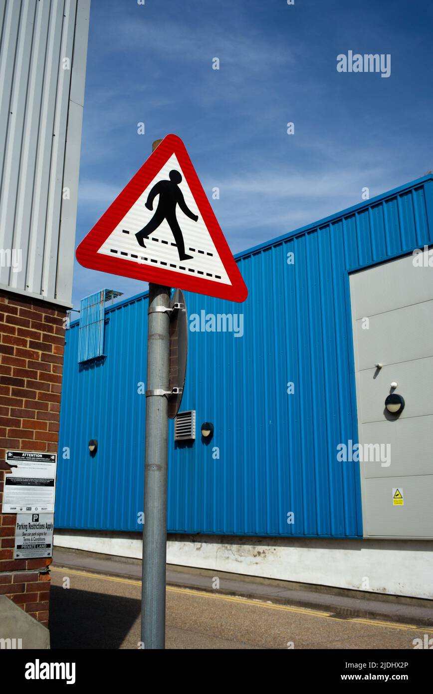 Ein rotes Warnschild für Fußgängerübergänge vor einem stark blauen Hintergrund moderner Industrieanlagen. Stockfoto