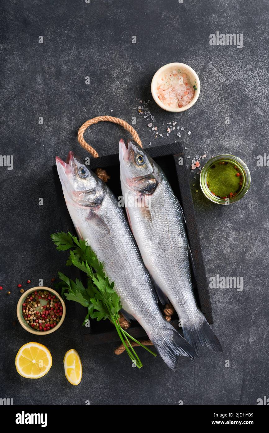 Seebarsch roh. Frischer Fisch-Bass mit Salz, Pfeffer, Petersilie, Olivenöl und Zitrone auf Schneidebrett auf dunklem Beton rustikalen Hintergrund. Essen kochen BA Stockfoto