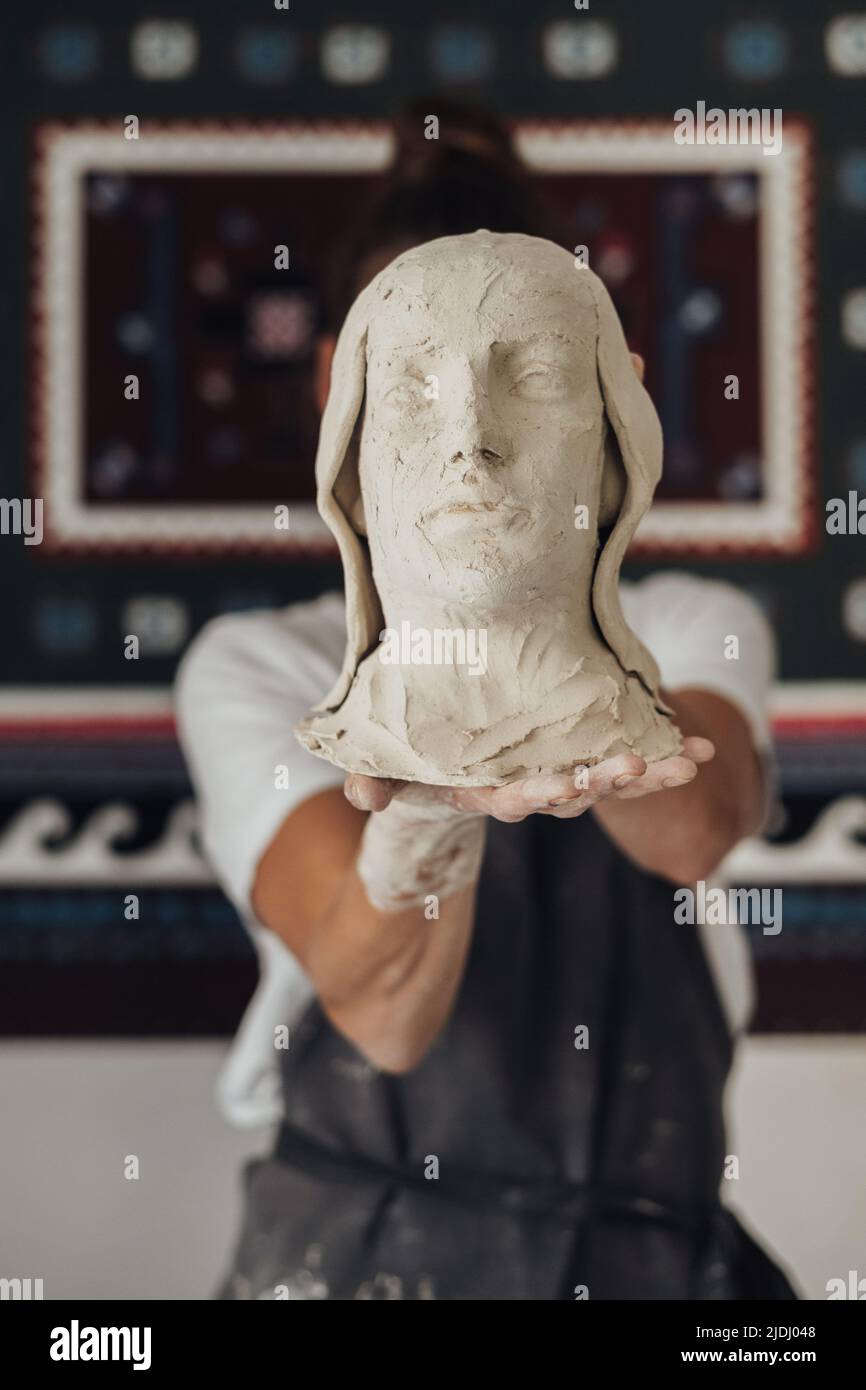 Weibliche Potter-Künstlerin, die aus ihrem Gesicht einen handgefertigten Kopf der menschlichen, künstlerischen Arbeit hält Stockfoto