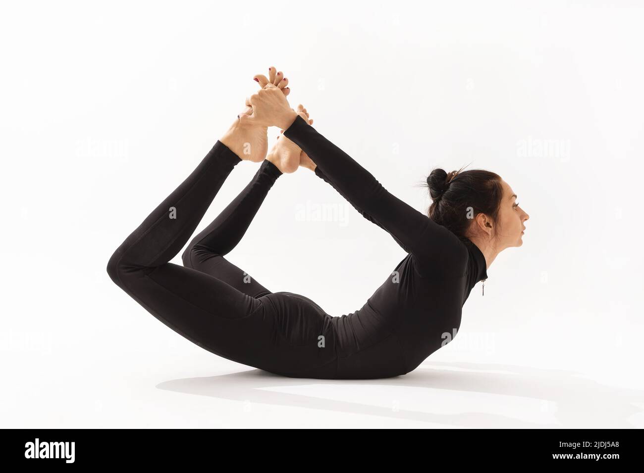 Eine Frau in schwarzer Sportkleidung, die Yoga praktiziert, führt eine dhanurasana-Übung in Bogenstellung auf weißem Hintergrund durch Stockfoto