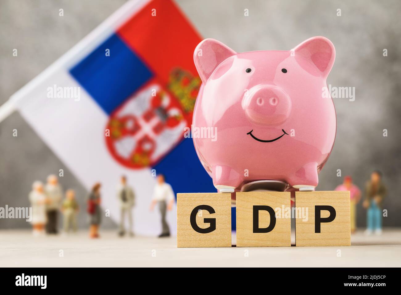 Sparschwein, Holzwürfel mit Text, Spielzeugleute aus Kunststoff und eine Fahne auf abstraktem Hintergrund, ein Konzept zum Thema serbisches BIP Stockfoto