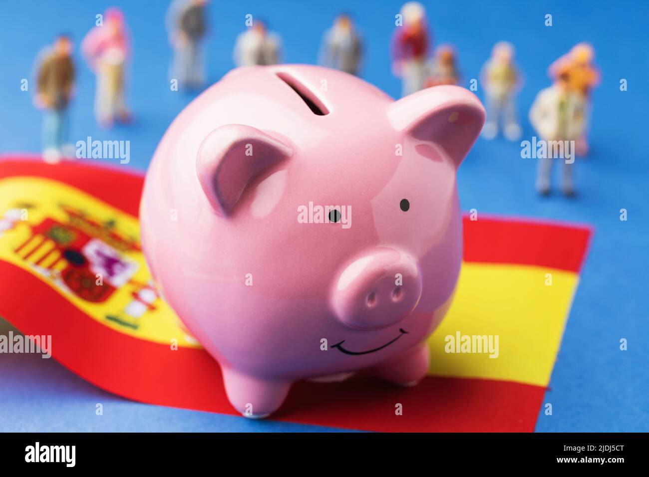 Sparschwein, Fahne und Plastikspielzeug auf farbigem Hintergrund, das Konzept des Einkommens der spanischen Bevölkerung Stockfoto