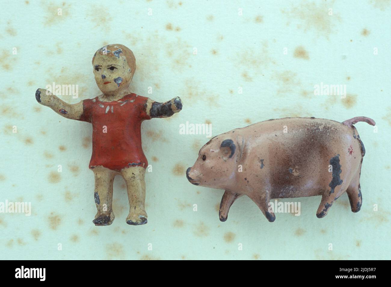 Abgenutzte Bleimodelle eines viktorianischen Kleinkindes mit ausgestreckten Armen und einem fulminanten Schwein, das auf antikem Papier liegt Stockfoto