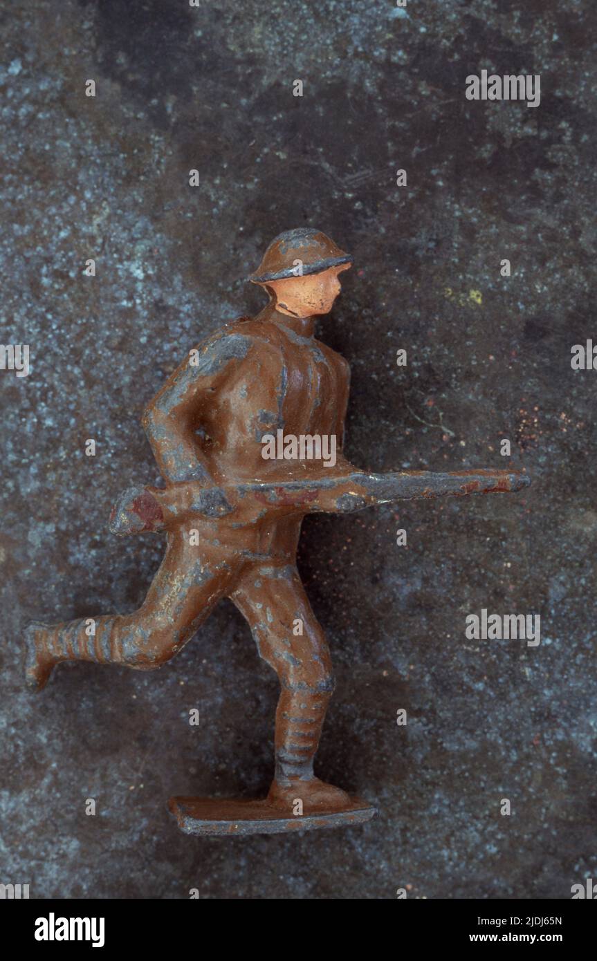 Abgenutztes Bleimodell des 1. Weltkrieges Armee Fußsoldaten, der mit Gewehr in Hüfthöhe gegen melierten Metallhintergrund läuft Stockfoto