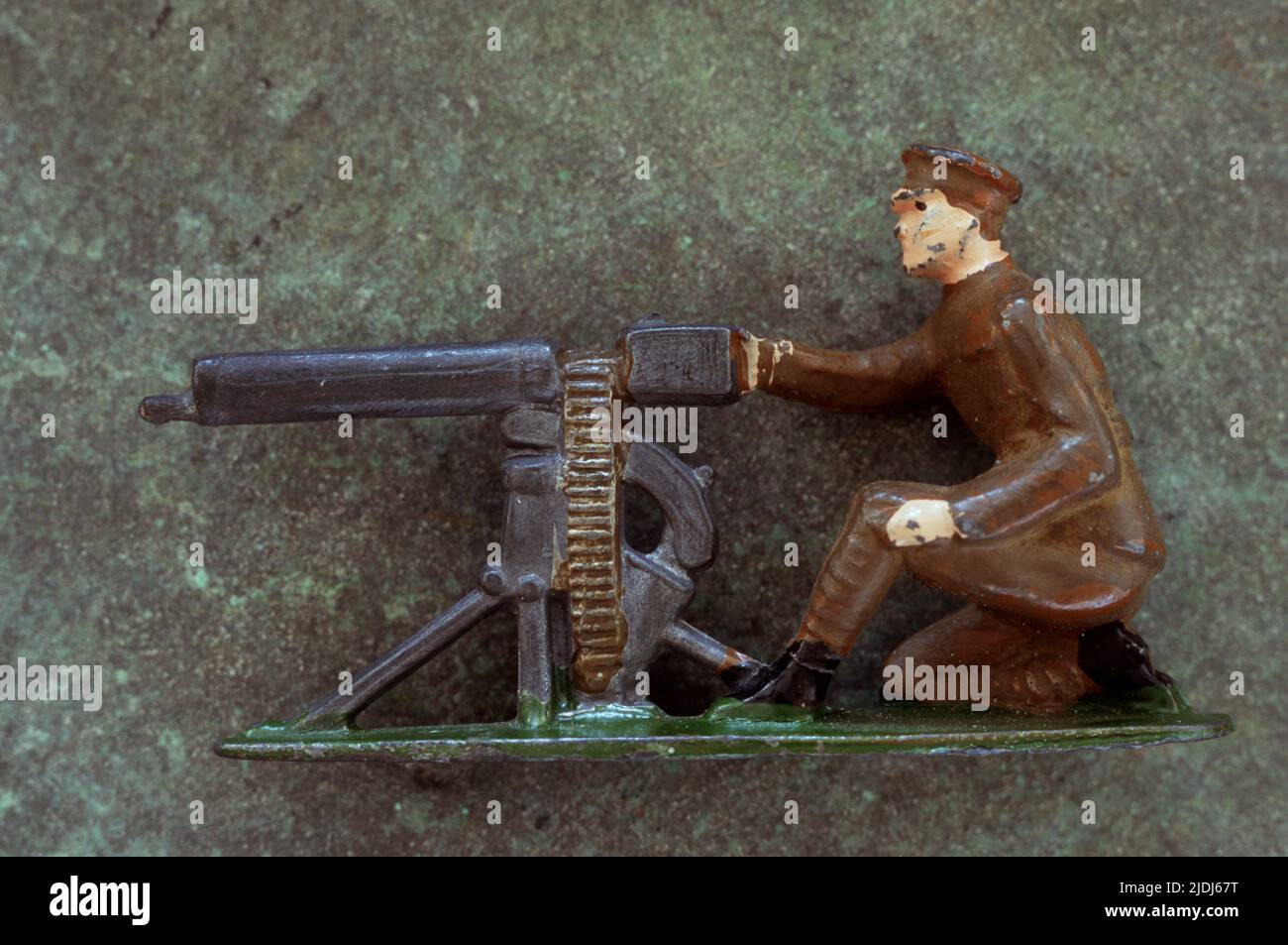 Abgenutztes Bleimodell des Soldaten der Armee aus dem 1. Weltkrieg, der vor einem Maschinengewehr vor meliertem Metallhintergrund kniete Stockfoto