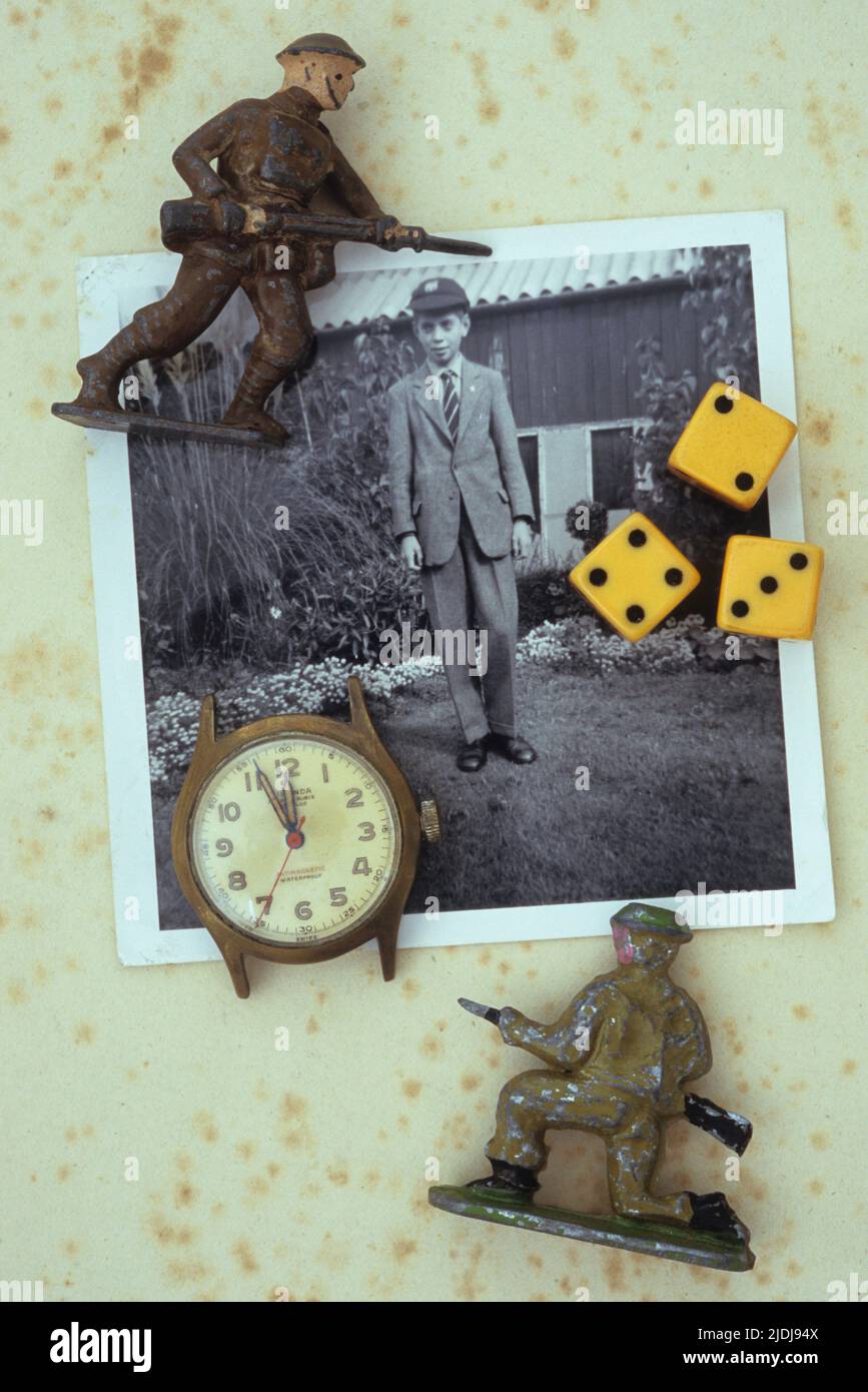 Vintage schwarz-weiß Foto von 1960s Jungen in Schuluniform und Mütze im Garten liegend mit alten Uhr drei Würfel und zwei Bleimodell Soldaten Stockfoto