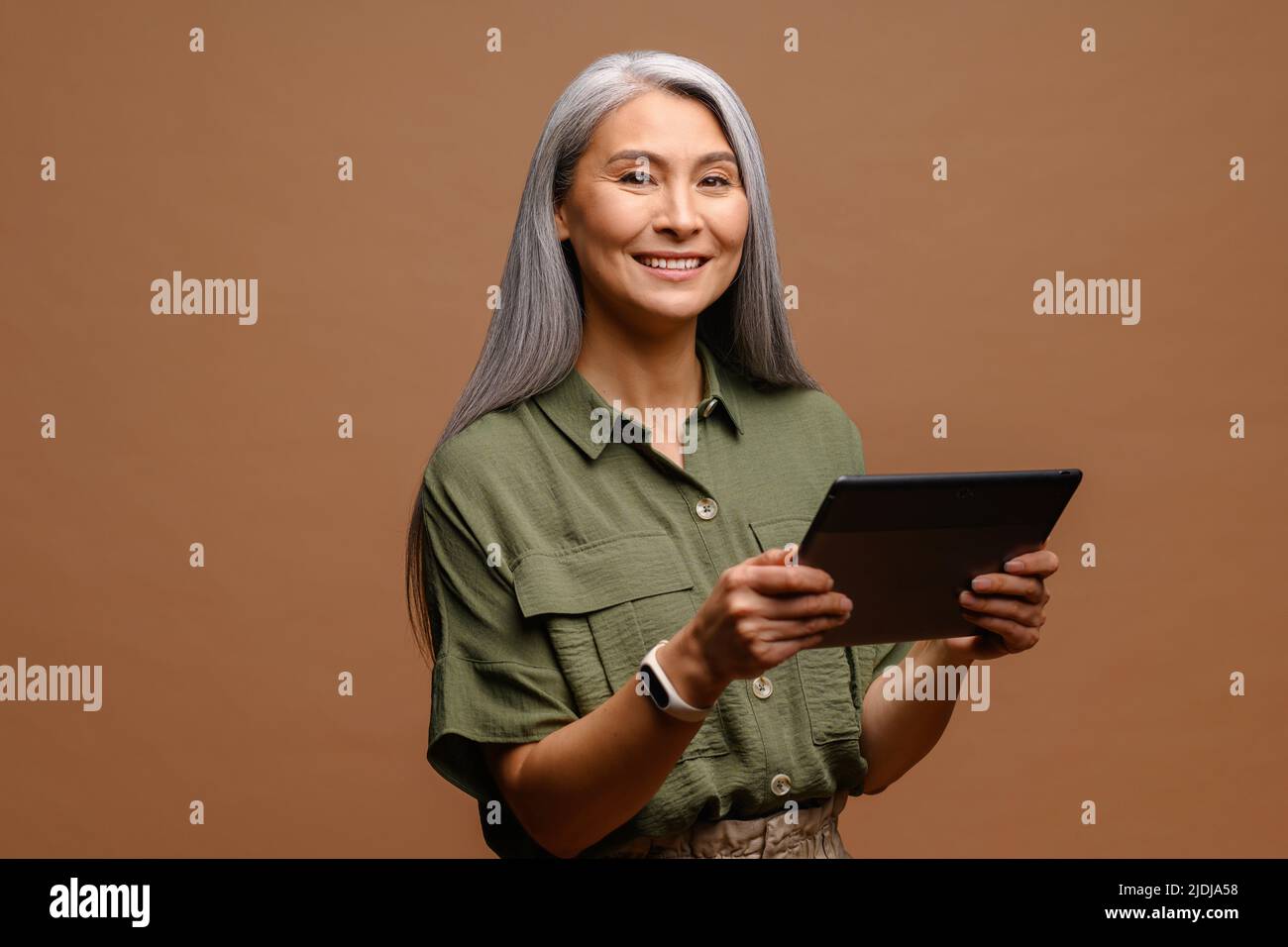 Moderne ältere Frau mit einem digitalen Tablet isoliert auf braun. Porträt einer reifen weiblichen Büroangestellerin, die Online-Technologie für Geschäftsabläufe nutzt, Computer-App für die Buchhaltung Stockfoto
