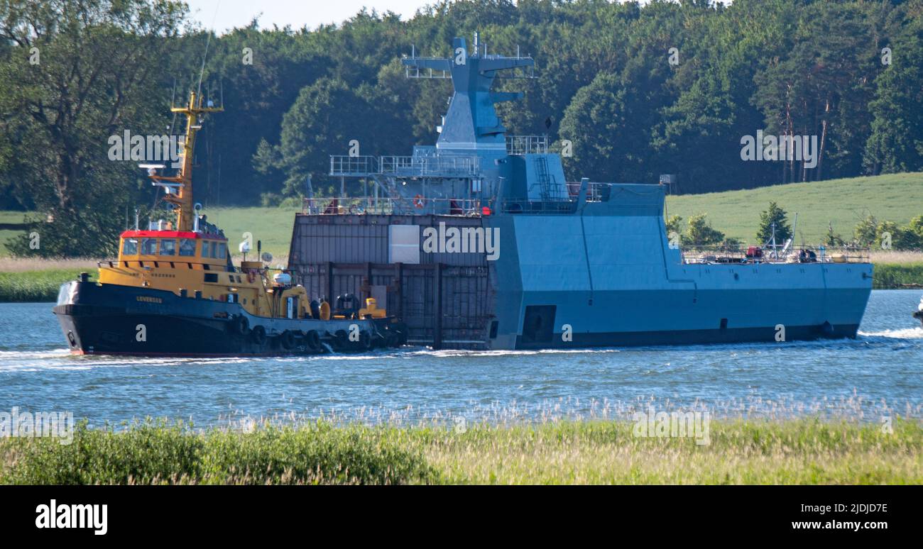21. Juni 2022, Mecklenburg-Vorpommern, Wolgast: Ein Rumpfsegment (Achterschiff) einer K130 Korvette wird von Schleppern vom NVL-Standort der Peene-Werft zum NVL-Standort Blohm Voss in Hamburg gebracht, um dort die andernorts gebauten Vorschiffe zu verbinden. Die ersten fünf Boote der neuen K130-Klasse sind bereits seit 2008 in Betrieb, fünf weitere folgen. Zwei der vier noch ausstehenden Kriegsschiffe werden derzeit ebenfalls ausgerüstet. Boot 9 befindet sich nach Angaben der Marineschiffe Lürssen (NVL) in der Produktionsphase, und Boot 10 hatte seinen Kiel Anfang dieses Jahres gelegt. Nach Angaben des Unternehmens, bei der Peene Stockfoto