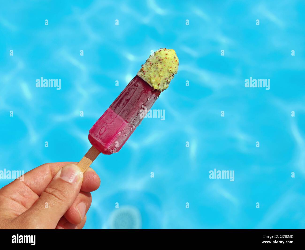 Die Hand hält fruchtige bunte Eiszapfen oder Wassereis vor einer blauen Pooloberfläche, helfen gegen Sommerhitze Konzeptbild Stockfoto