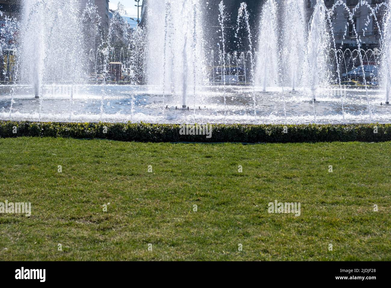 Brunnen im Stadtzentrum. Wasserstrahlen schmücken einen runden Stadtplatz, einen kleinen Teich und Gras, sonnige Tage, Nahaufnahme Stockfoto