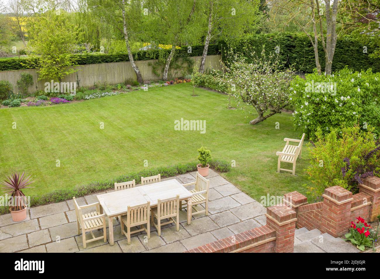 Gartenterrasse mit Gartenmöbeln auf einer Terrasse in einem von Großbritannien gestalteten Garten mit großer Liegewiese Stockfoto