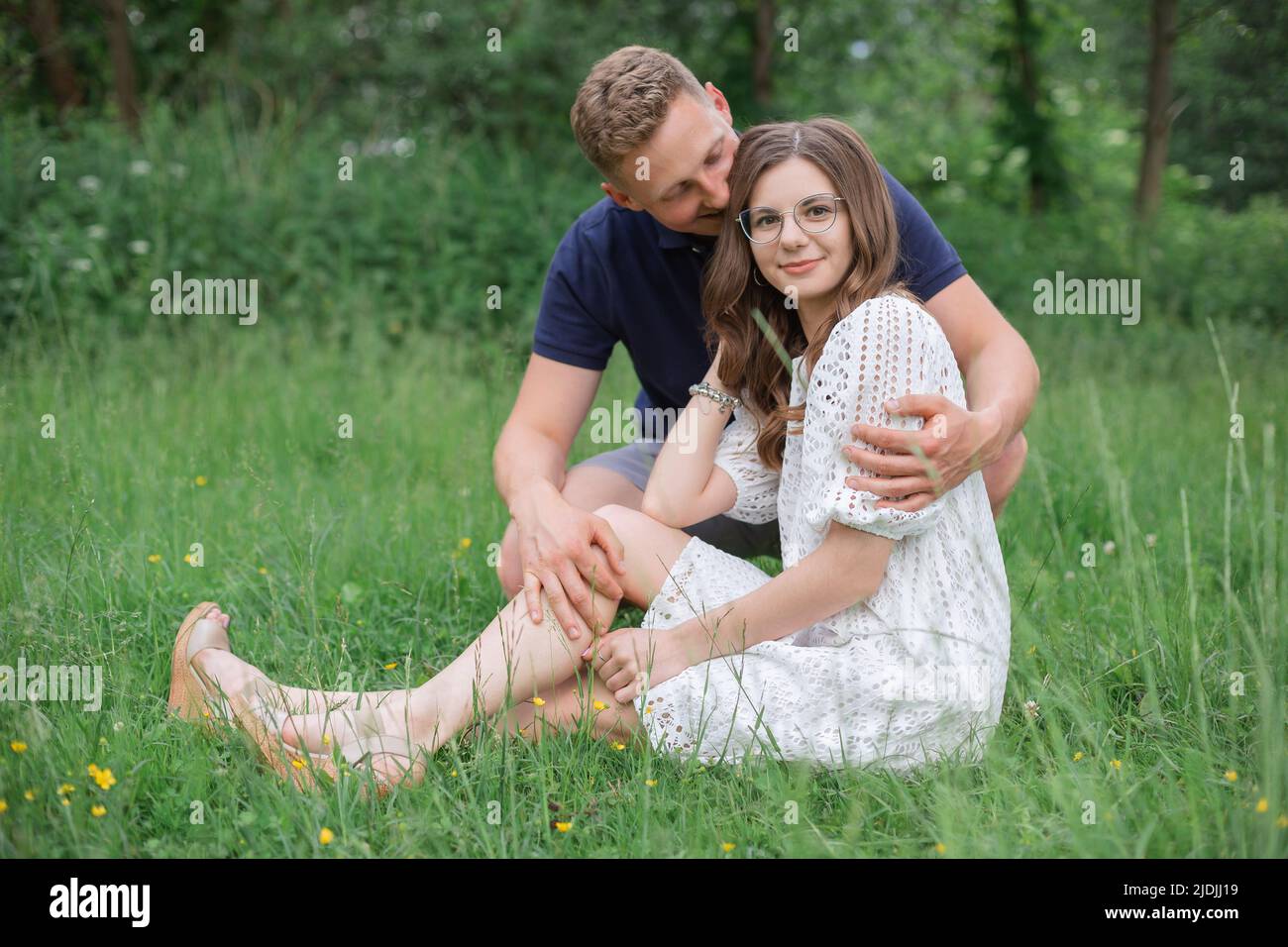 Liebevolles junges Paar, das im Park auf Gras sitzt und sich küsst. Junge Männer und Frauen genießen den Sommertag. Glückliche Menschen in der Liebe, Honigmond Stockfoto